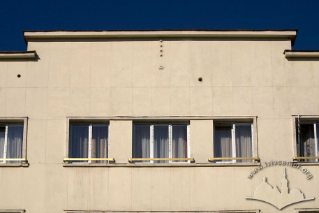 Просп. Свободи, 5. Центральна частина фасаду в рівні IV-го пов. з мінімалістичним віконним обрамленням і жардиньєрками та аттиком
